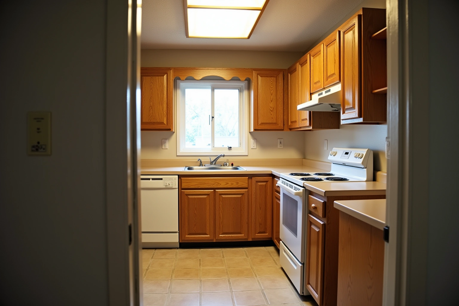 Dated kitchen with honey oak raised-panel cabinets, beige laminate counters, white range and dishwasher, and a fluorescent ceiling box.